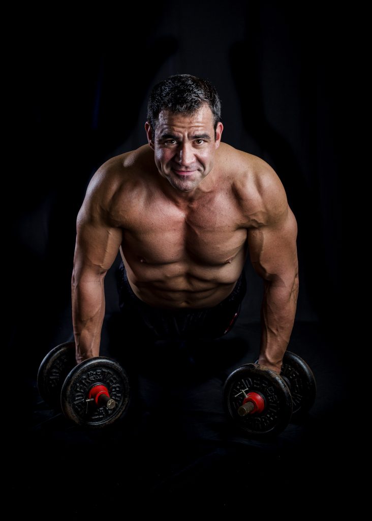 Man posing for a fitness photographer holding a plank with dumbbells