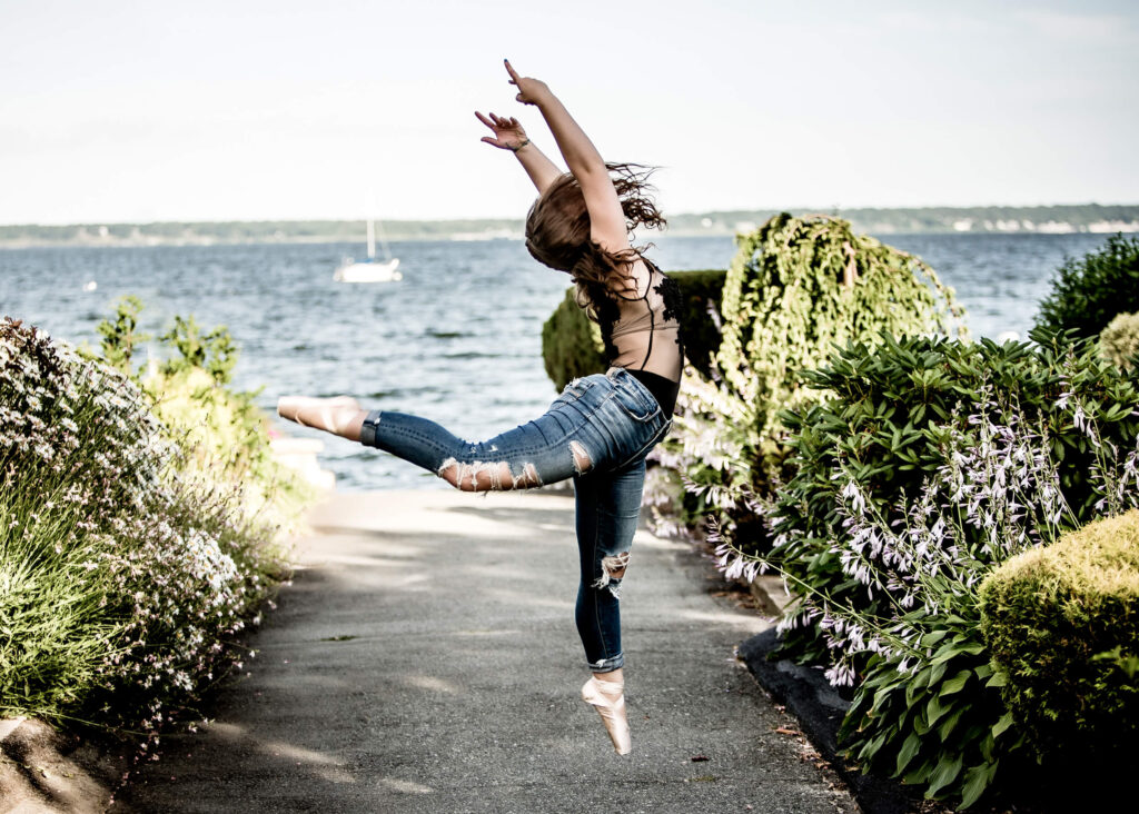 high school senior girl dancing on toe shoes near the ocean for senior portraits