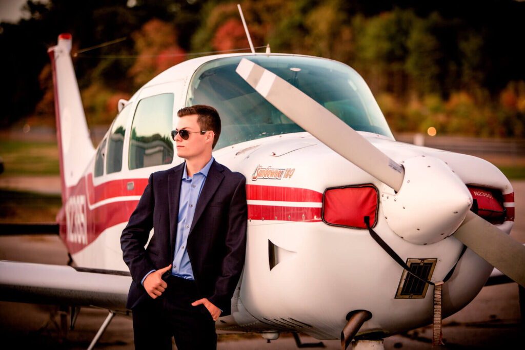 HS senior wearing a suit leaning on a prop plane for a senior photographer