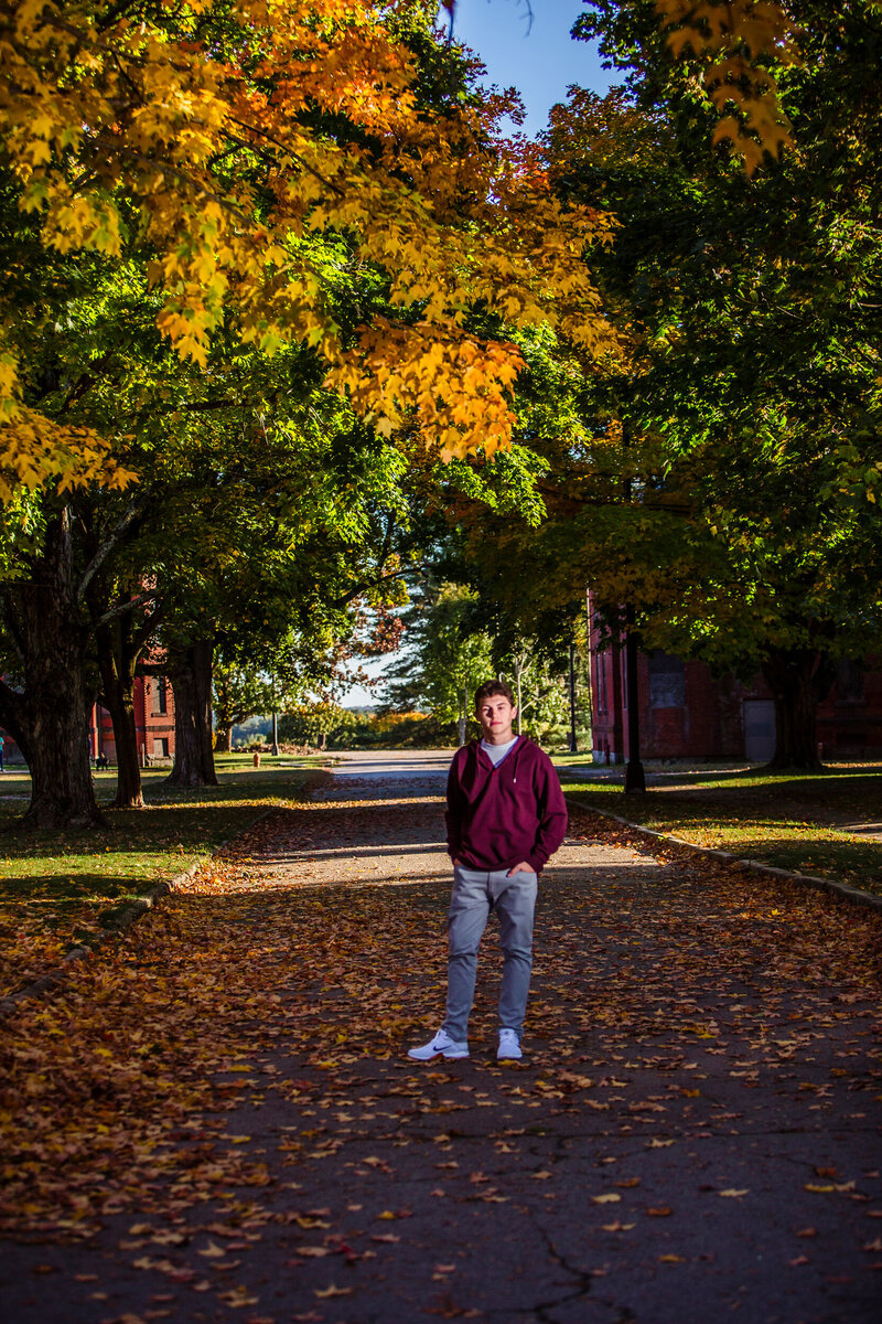 HS senior boy standing between trees with fall foliage
